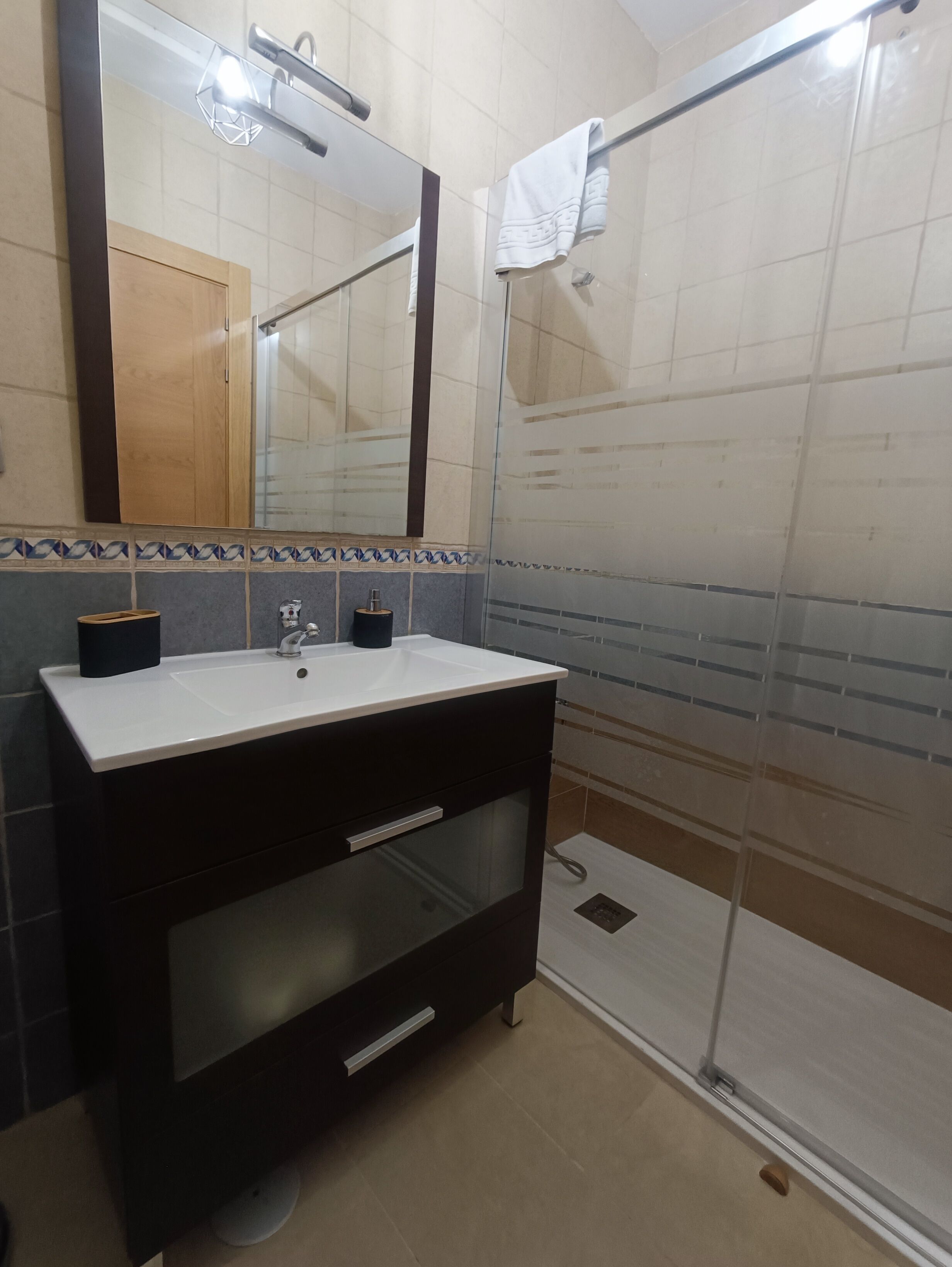 Un baño moderno con un espejo grande, un lavamanos, tocador y cabina de ducha con mampara de vidrio.