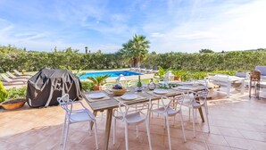An outdoor dining area with a pool view, white chairs, and a grill cover labeled "hyla". - Villa Miravall Selva by Balearic Villas (Selva)