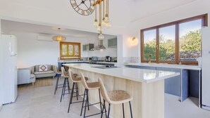 A modern kitchen with a large island, bar stools, and a hanging light fixture. - Villa Miravall Selva by Balearic Villas (Selva)