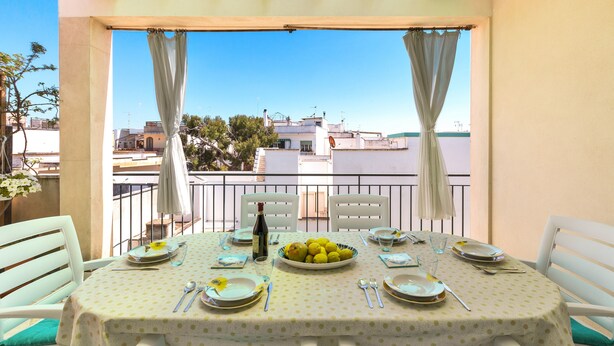 Une table de balcon, dressée avec des assiettes, des couverts et une bouteille, d’où l’on peut admirer le panorama de la ville.