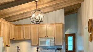 A kitchen with wooden cabinets, a white refrigerator, a microwave, a stove, and a dining area with stools. - THE PERCH-Beach Cottage- FREE GOLF CART-Just Minutes from the Gulf/BEACH! (Panama City Beach)