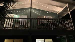 A two-story building with a balcony, string lights, and a palm tree. - THE PERCH-Beach Cottage- FREE GOLF CART-Just Minutes from the Gulf/BEACH! (Panama City Beach)