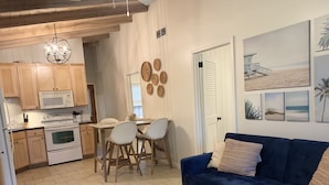 A modern kitchen with wooden cabinets, a white microwave, and a stove. There is a dining area with a table and chairs. A blue sofa and a coffee table are in the living area. - THE PERCH-Beach Cottage- FREE GOLF CART-Just Minutes from the Gulf/BEACH! (Panama City Beach)