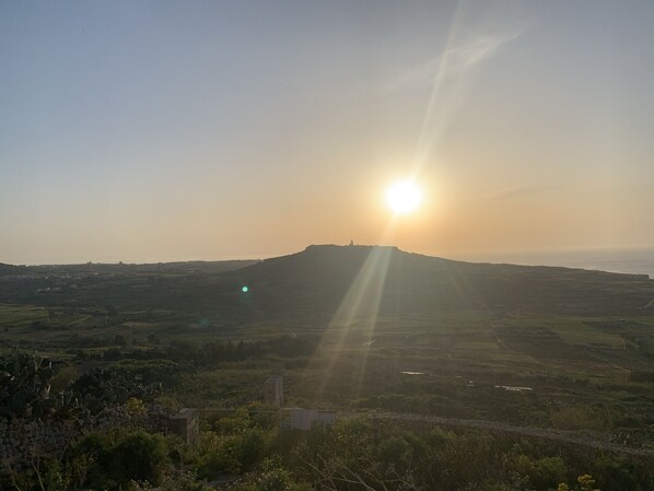 A landscape with a sun setting behind a hill, casting long shadows across the terrain. - Heritage Living Apartment With Spectacular Views (Zebbug)