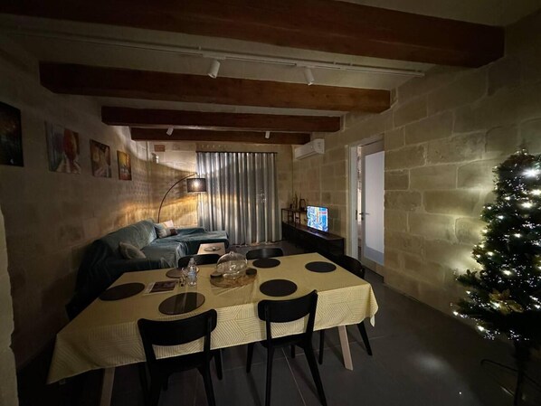 Un comedor acogedor con una mesa preparada para cuatro personas, un árbol de Navidad y un televisor al fondo.