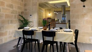 A dining area with a stone wall, a wooden ceiling, and a kitchen in the background. - Heritage Living Apartment With Spectacular Views (Zebbug)