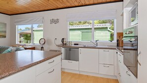 Een moderne keuken met witte kasten, granieten aanrechtbladen en een houten plafond.