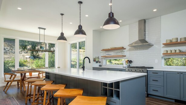A modern kitchen with a large island, bar stools, pendant lighting, and a view of the outdoors.