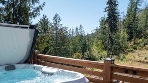 A hot tub with a wooden deck and a forest view.
