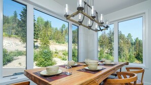 A dining area with a wooden table set for four, large windows offering a view of a forested landscape.