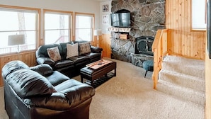 A spacious living room with a stone fireplace, a black leather sofa, and a wooden staircase. - Stunning lake house with private dock (Joseph)