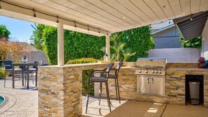 En uteplats med en grill av sten och metall, en sittgrupp och en pergola dekorerad med ljusslingor.