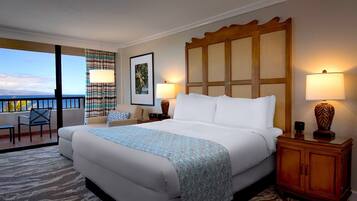 A hotel room with a large bed, a balcony with a view, a desk with a chair, and a wooden cabinet.