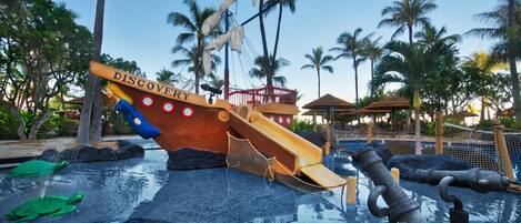Uma área de recreação com água, incluindo um escorregador com tema de navio e uma piscina decorada com uma tartaruga.