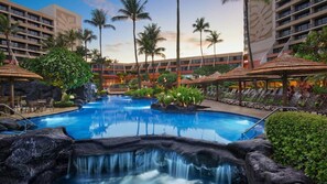 Ein Hotelpool mit Wasserfall, Palmen und Liegestühlen.
