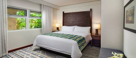 Ein Hotelzimmer mit Bett, Deckenventilator, Fenster mit Vorhängen, einem an der Wand befestigten Fernseher und einem gerahmten Bild.