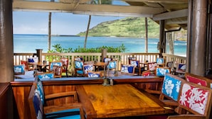 Un restaurant situé en bord de mer, avec des tables et des chaises en bois, une vue sur l’océan et une terrasse en bois.
