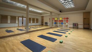 A spacious room with a large mirror, wooden flooring, and exercise mats arranged for yoga or stretching.