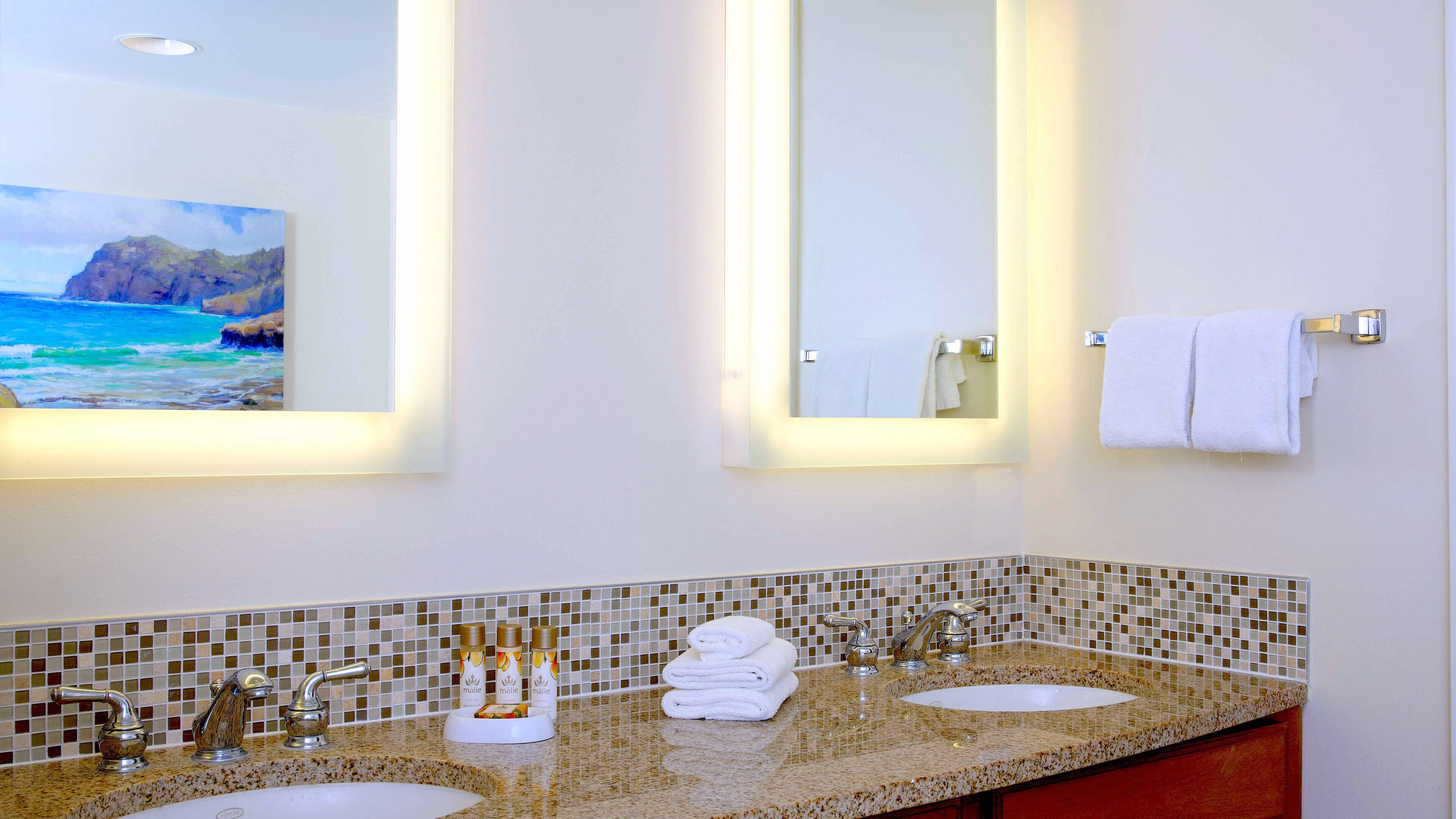 A bathroom with two sinks, a large mirror, and a painting of a beach scene.