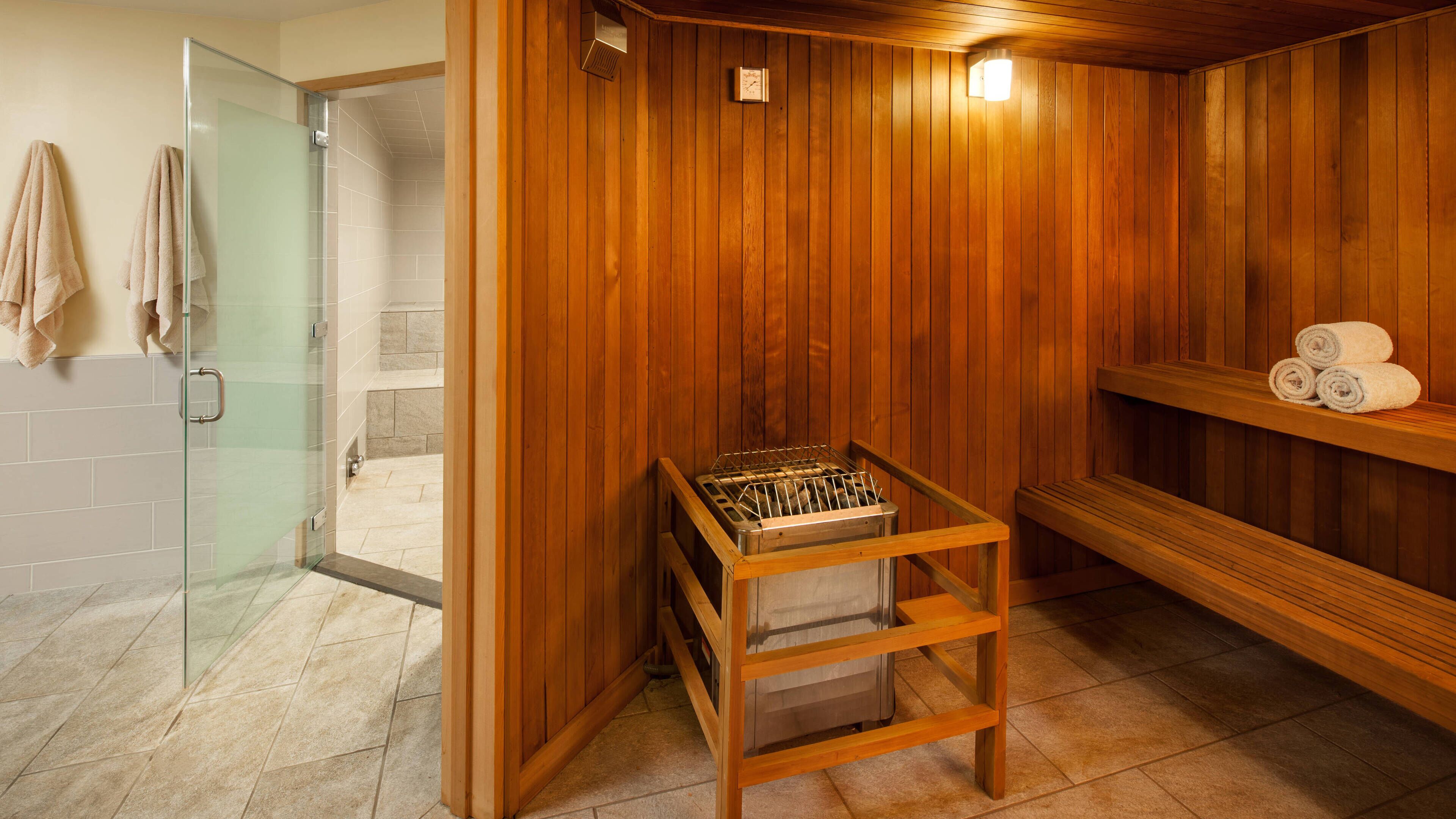 Een sauna met houten wanden, een glazen douchecabine en een bank met handdoeken.