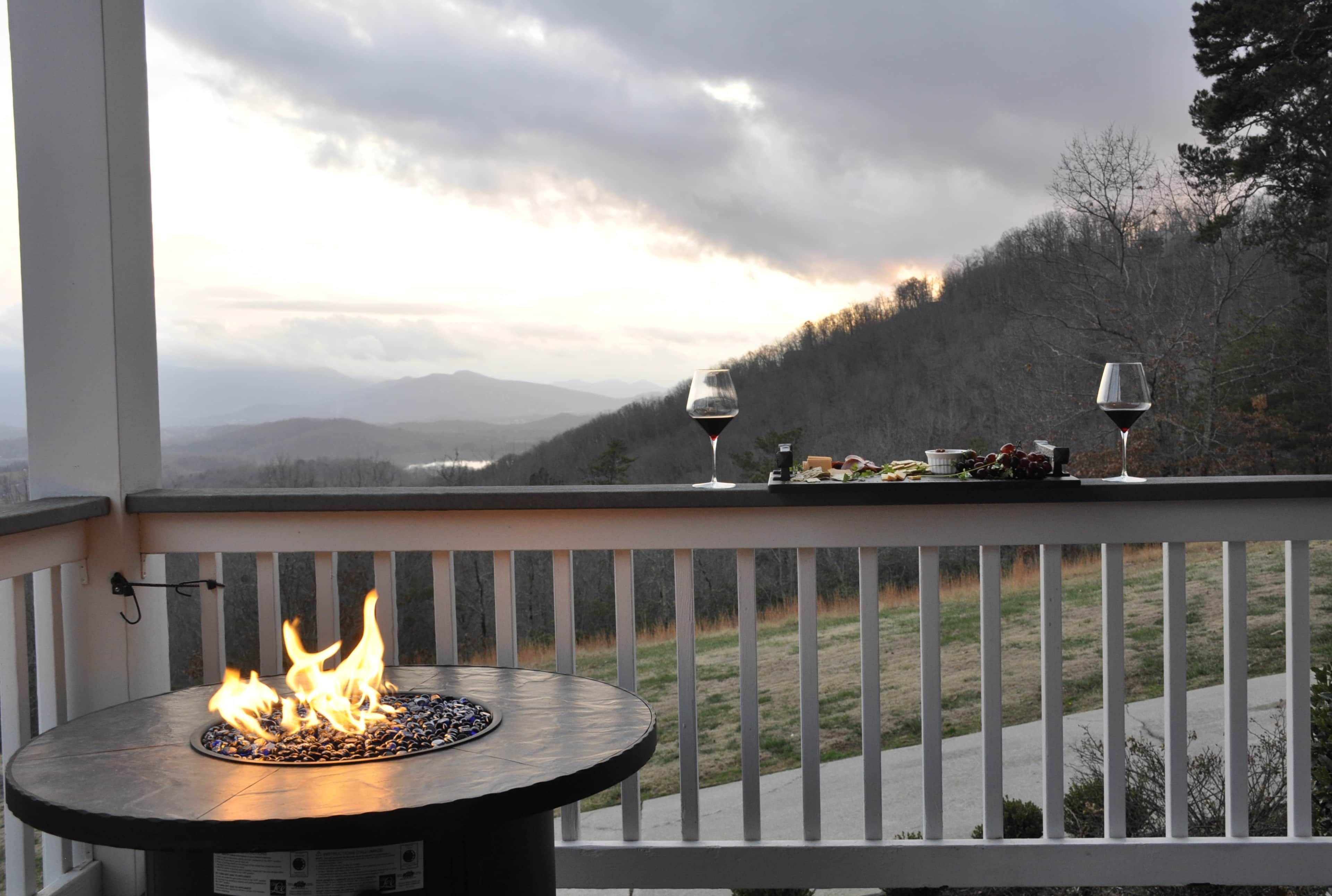 Un balcon agrémenté d’un foyer, deux verres à vin et une table avec de la nourriture et des boissons.