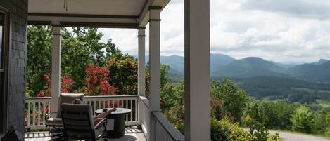 A covered porch with a table and chairs, overlooking a mountainous landscape.