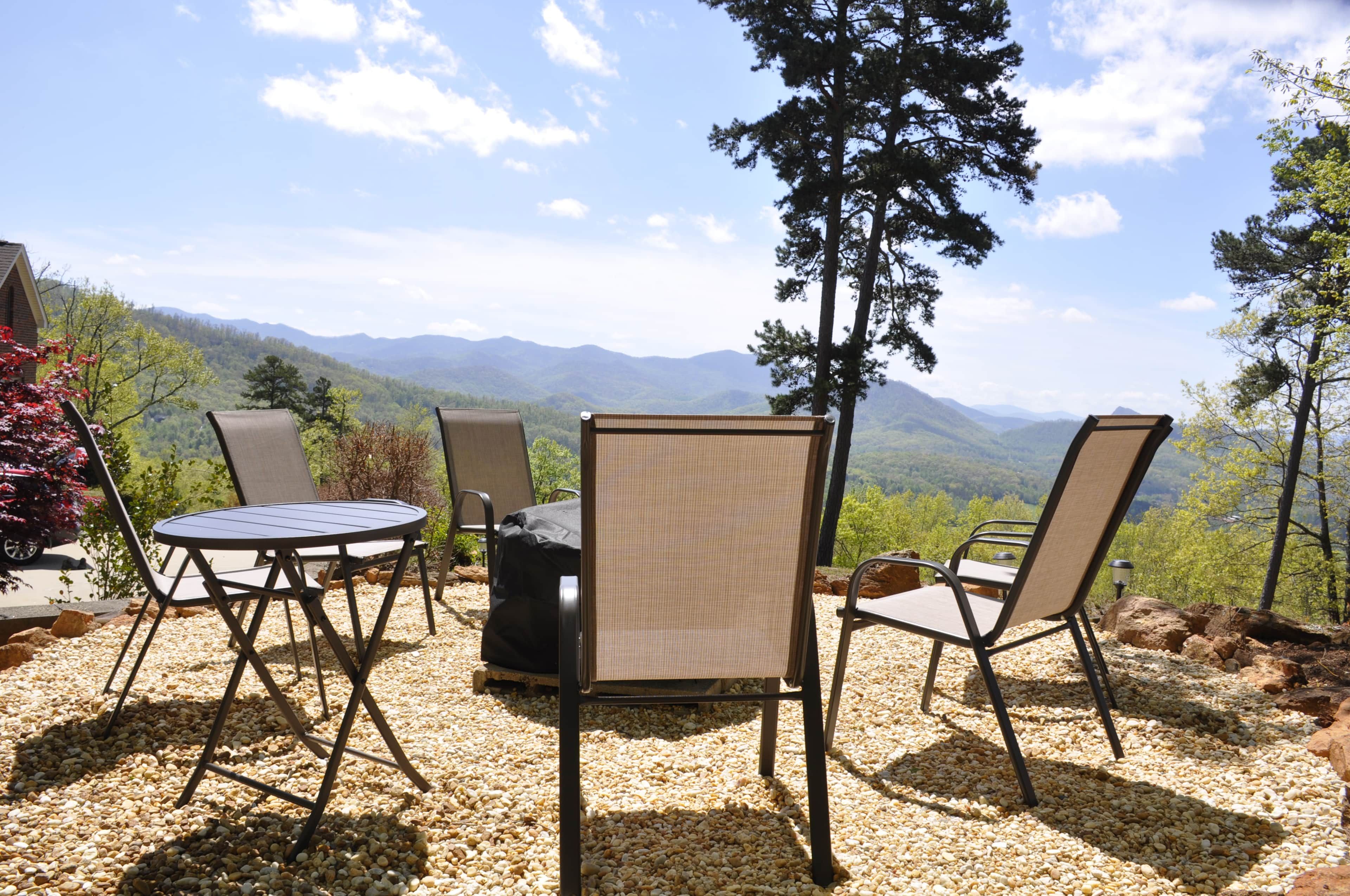 Un área de estar al aire libre con una mesa y sillas, rodeada de grava, y vista a la montaña al fondo.