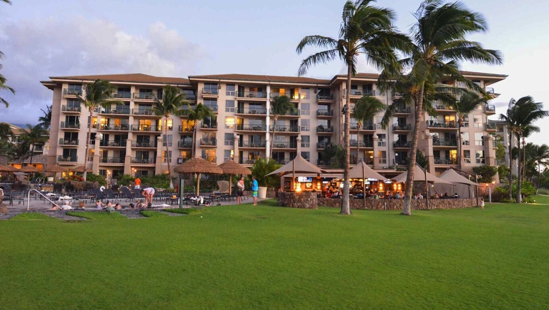 A multi-story hotel with balconies, outdoor seating, and palm trees.