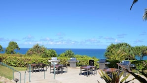 Patio esterno con tavoli e sedie, un barbecue e vista sull'oceano.