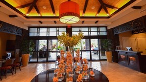 A lobby with a reception desk, a large window with a view of the outside, and a central table with flower arrangements.