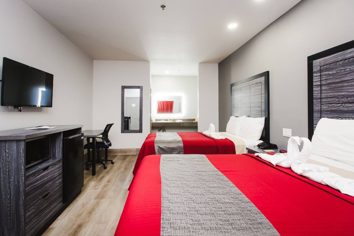 A hotel room with two beds, a desk, a TV, and a mirror.