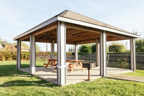 A covered outdoor pavilion with a wooden roof and metal columns, equipped with picnic tables and a grill. - Palace Inn Baytown Spur TX-330 (Baytown)