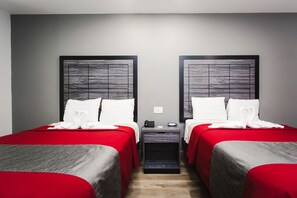 A hotel room with two beds, each with a red bedspread and white pillows. There is a nightstand between the beds with a phone and a small table. - Palace Inn Baytown Spur TX-330 (Baytown)