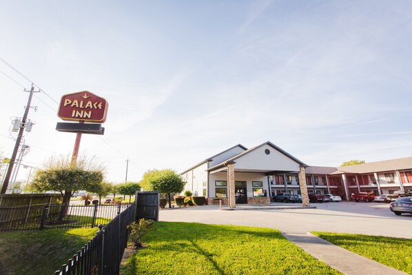 A hotel with a sign reading "Palace Inn," a parking lot, and a building with a flat roof. - Palace Inn Baytown Spur TX-330 (Baytown)
