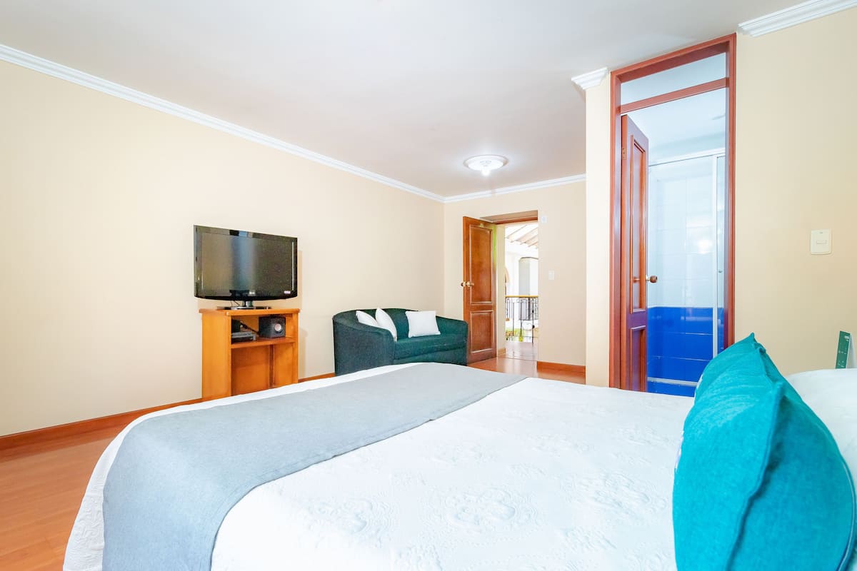 Ein Hotelzimmer mit einem Bett, einem Fernseher auf einem Holzständer, einem grünen Sofa und einer Tür, die auf einen Balkon führt.