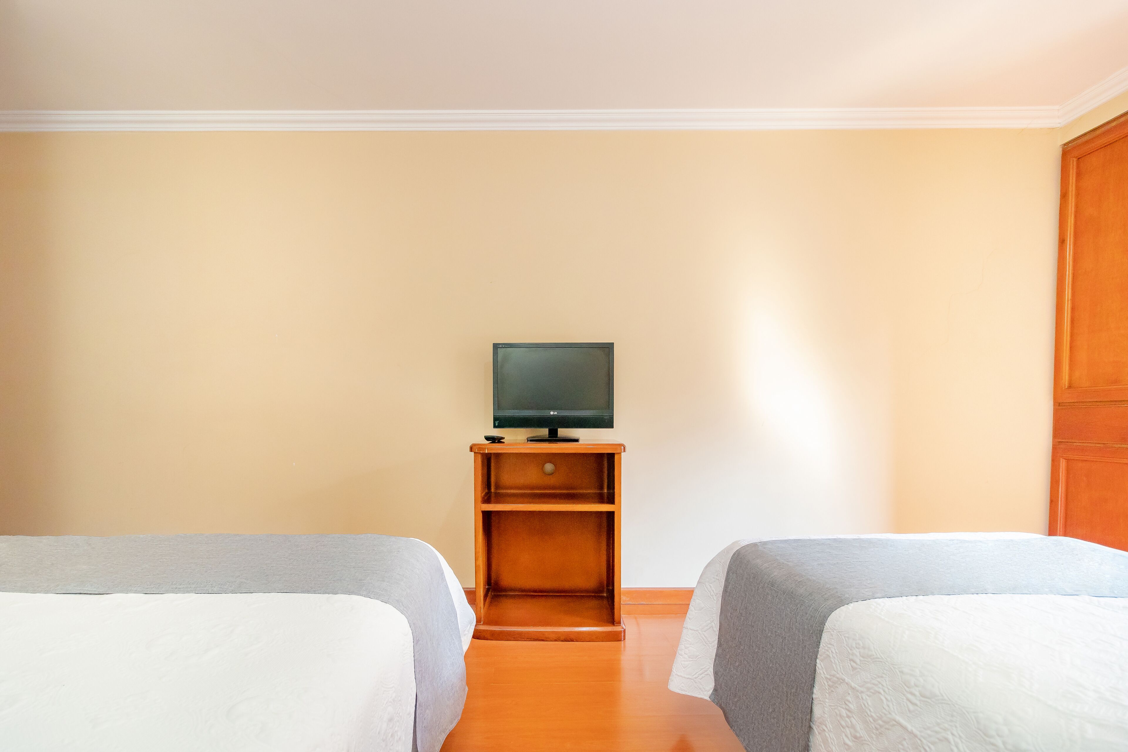 A hotel room with two beds, a wooden nightstand with a television, and a plain wall.