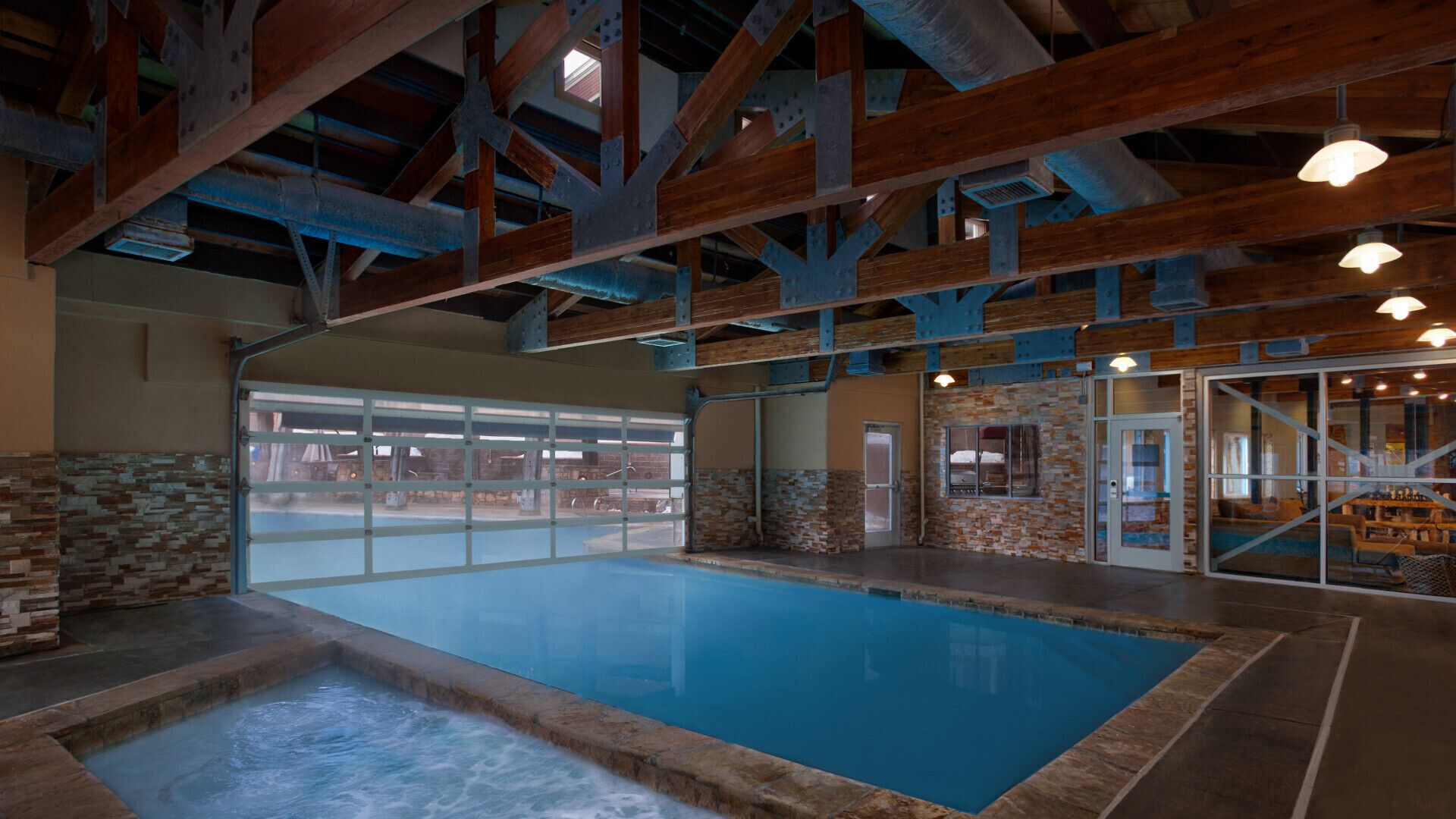 An indoor swimming pool with a stone wall and a view of the outside.