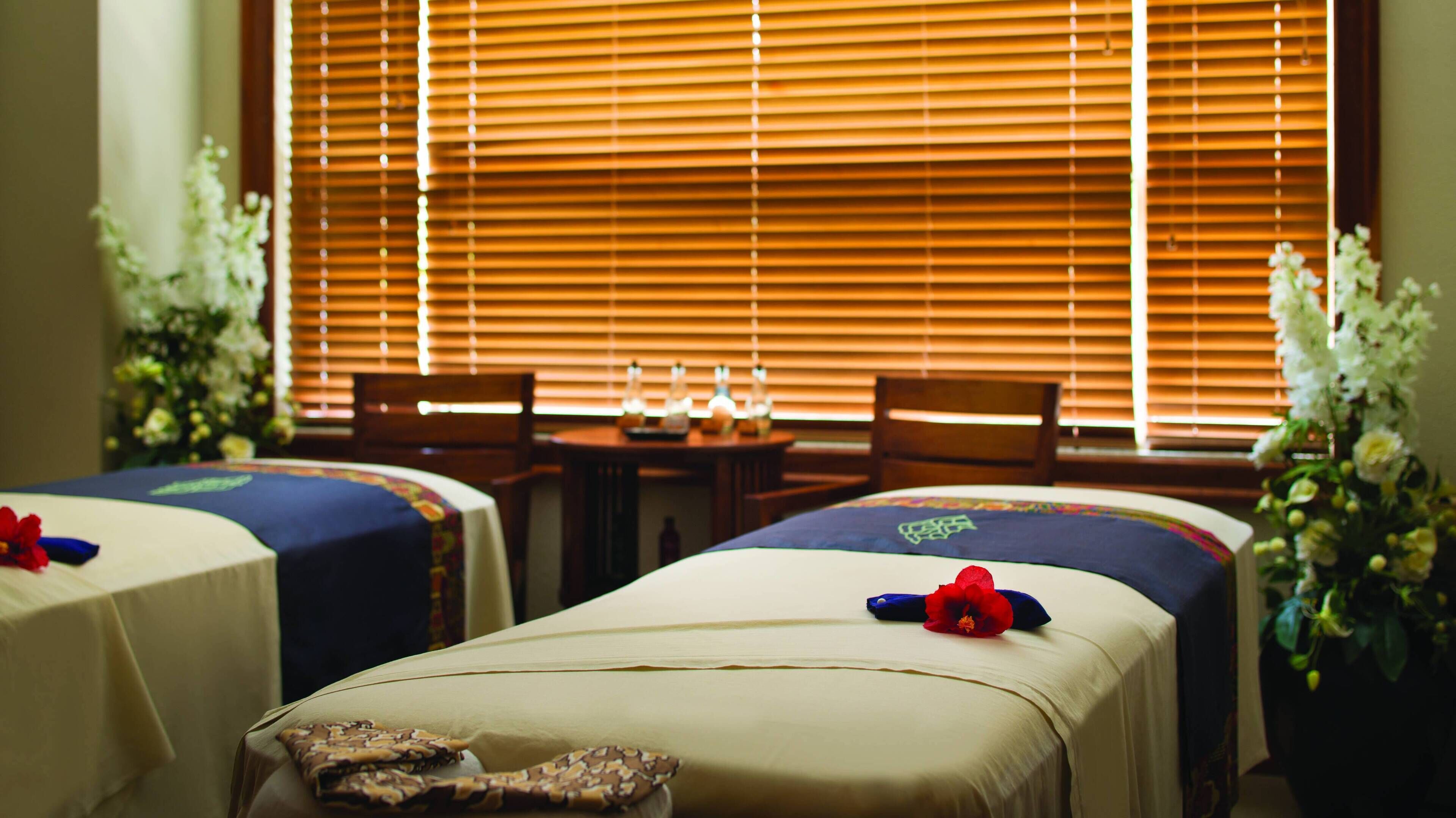 Two single beds with floral headboards, a wooden table with candles, and a window with blinds.