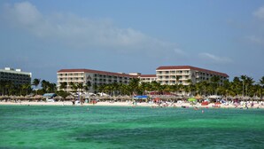 Een strandhotel met meerdere balkons, palmbomen en strandparasols.