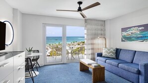 Een moderne hotelkamer met balkon en uitzicht op zee, een plafondventilator, een flatscreen televisie en een bank.