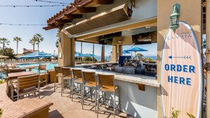 An outdoor bar area with a pool view, bar stools, and a sign indicating an order point.
