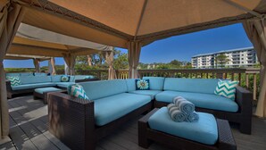 A covered outdoor seating area with wicker furniture and blue cushions, overlooking a residential area.