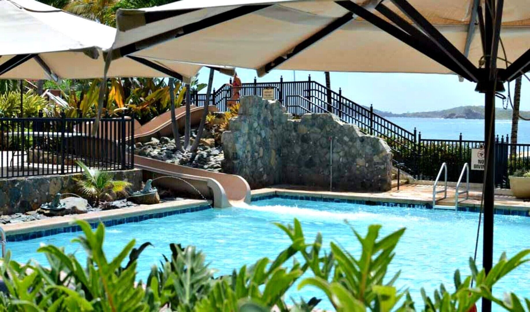 Zona de piscina con tobogán, pared de piedra y vistas al mar.