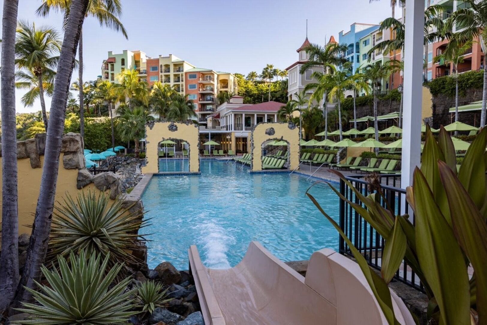 Ein Resort-Pool mit Rutsche, umgeben von Palmen und Blick auf bunte Gebäude.