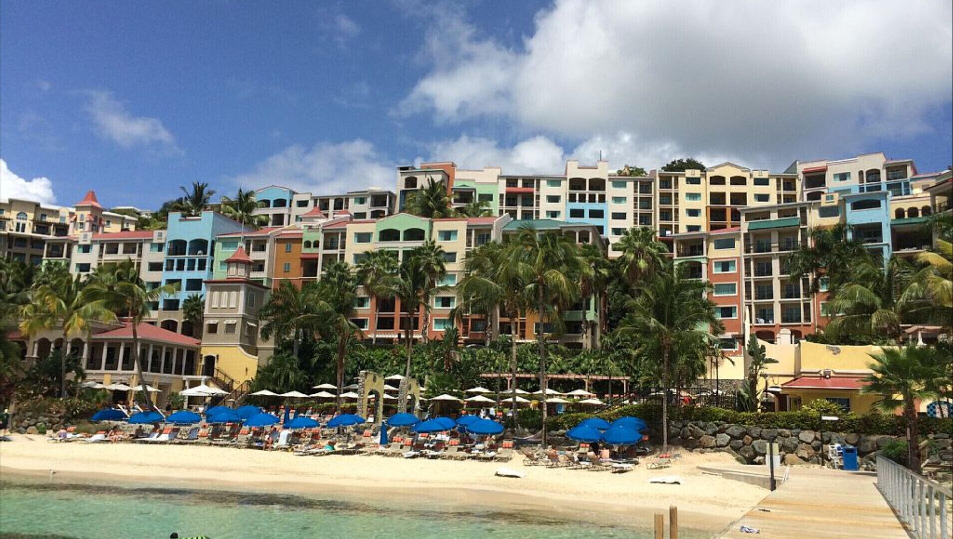 Ein Hotel direkt am Strand mit farbenfrohen Gebäuden, einem Sandstrand und Palmen.