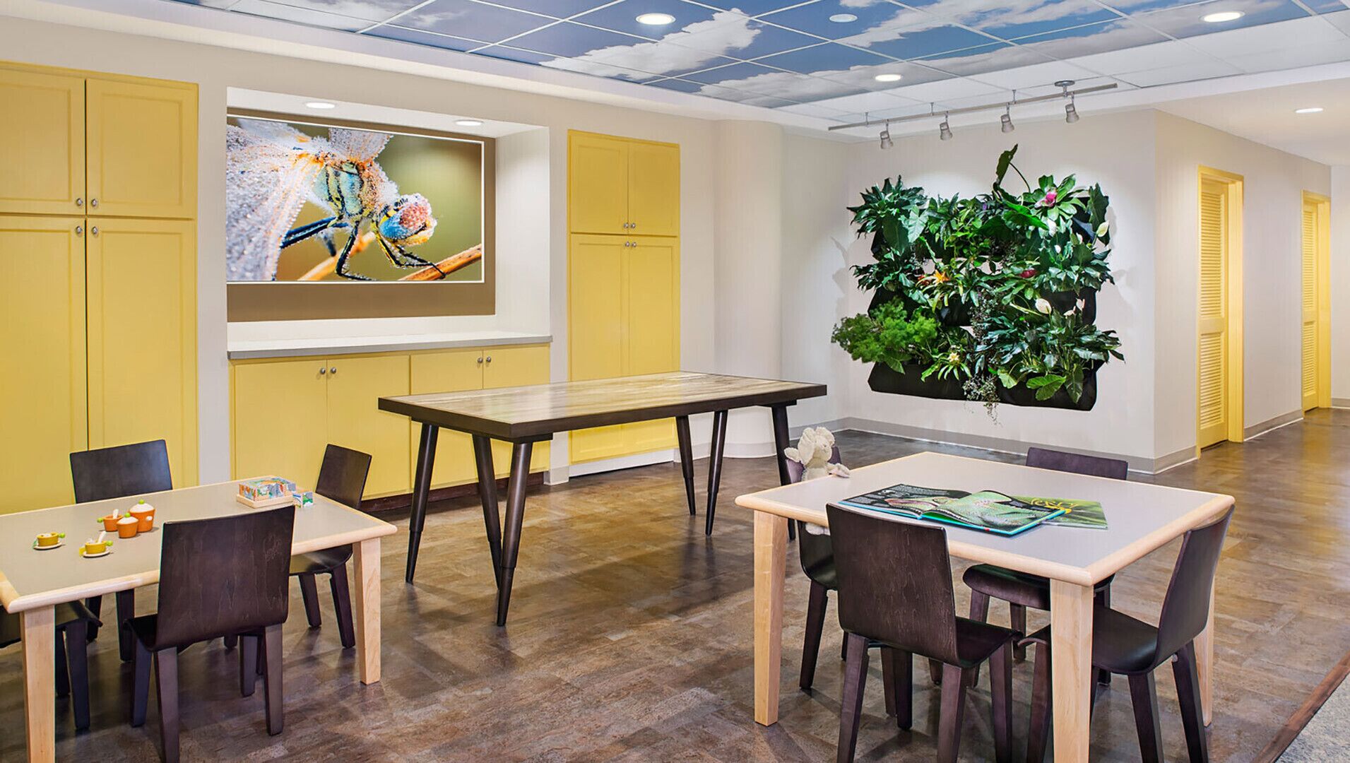 Una sala conferenze moderna con armadietti gialli, un grande dipinto di una libellula e un giardino verticale.