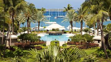 Un resort con piscina centrale, circondato da palme e vista sul mare con barche.