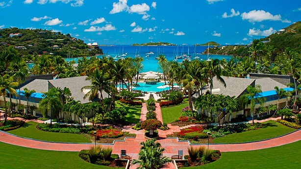 A resort with a central pool, palm trees, and a view of the ocean.