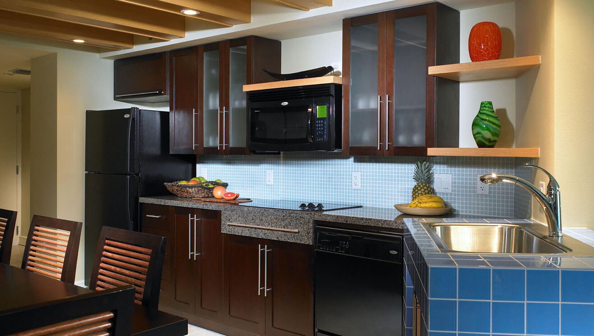 A modern kitchen with dark wooden cabinets, a black microwave, and a stainless steel sink.