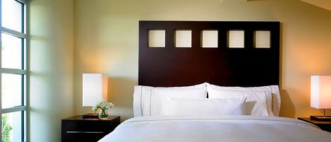 A hotel room with a large bed, two bedside tables, a dark headboard, and a window on the left.